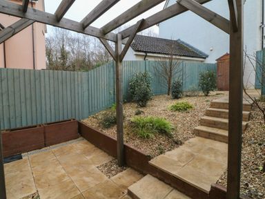 A backyard with tiled patio steps wooden pergola fenced garden with shrubs and storage shed at Reubens Cottage in Fremington Devon