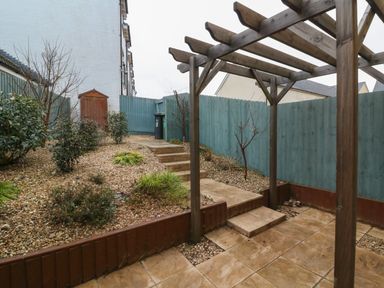 A backyard with tiled patio wooden pergola stone steps small plants and a blue wooden fence at Reubens Cottage in Fremington Devon
