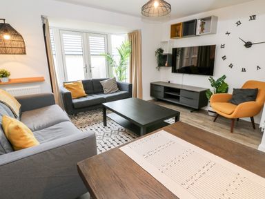 A living room with two gray sofas a yellow armchair a black coffee table a wall-mounted tv and large clock at 20 Bishops Way in Falmouth