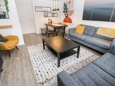 A living room with a coffee table on a patterned rug and a dining table with chairs and a bench at 20 Bishops Way in Falmouth
