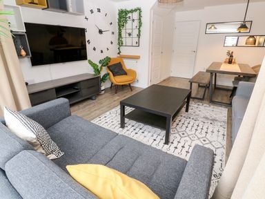 A living room with a large wall clock a yellow armchair and a dining table at 20 Bishops Way in Falmouth