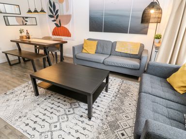 A living room with two grey sofas yellow cushions a black coffee table and a dining table with bench at 20 Bishops Way in Falmouth
