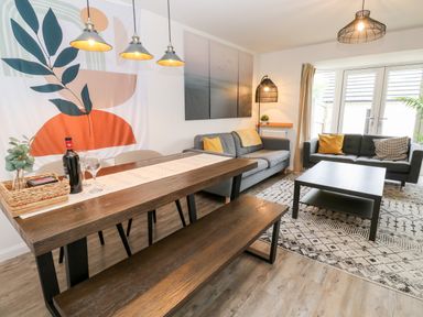 A living room and dining area with two sofas a wooden table and bench at 20 Bishops Way in Falmouth