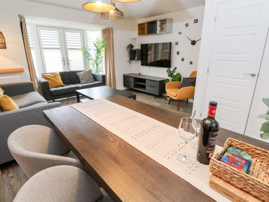 A living room with a dining table a wine bottle and glasses sofas a TV and an armchair at 20 Bishops Way in Falmouth