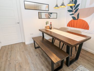 A dining area with a wooden table and bench two chairs pendant lights and wall art at 20 Bishops Way Falmouth