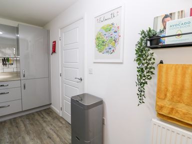 A kitchen corner with gray cabinets knives on the wall a gray trash bin a door a yellow towel a plant and cookbooks at 20 Bishops Way in Falmouth