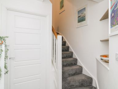 A stairway with gray carpet leading upward next to a white door and wall with framed pictures and a bowl on a shelf at 20 Bishops Way in Falmouth