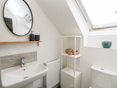 A bathroom with a sink mirror toilet shelf with baskets and a window at 20 Bishops Way in Falmouth