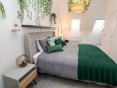 A bedroom with a bed featuring green and grey bedding and pillows with plants hanging on the wall at 20 Bishops Way in Falmouth