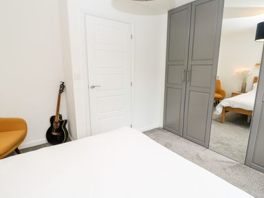 A bedroom with a white bedspread grey wardrobe with mirrored door a black acoustic guitar and an orange chair at 20 Bishops Way in Falmouth