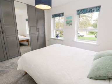A bedroom with a bed white bedding green pillows gray wardrobes and two windows at 20 Bishops Way Falmouth