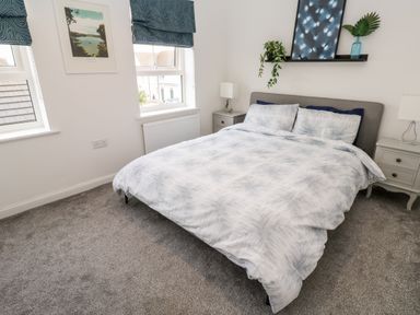 A bedroom with a double bed between two bedside tables with lamps and a shelf with plants above the bed at 20 Bishops Way in Falmouth