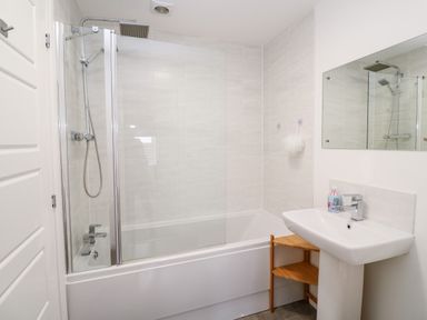 A bathroom with a bathtub and shower next to a sink with a mirror above at 20 Bishops Way in Falmouth