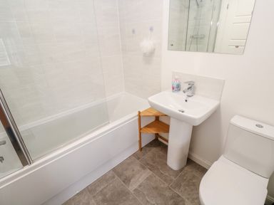 A bathroom with a bathtub shower combination a pedestal sink a toilet and a small wooden corner shelf at 20 Bishops Way in Falmouth