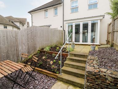 A small backyard garden with a wooden table and chairs concrete steps flower beds and patio doors at 20 Bishops Way in Falmouth