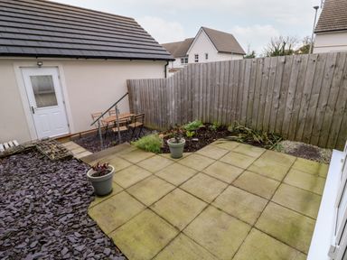 A small backyard with a paved patio, potted plants, a wooden fence, and a table with chairs at 20 Bishops Way in Falmouth