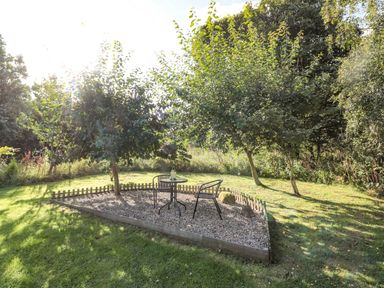 An outdoor garden area with two trees a small fenced gravel section with a round table and two chairs at Evergreen Lodge Felmoor Holiday Park near Felton