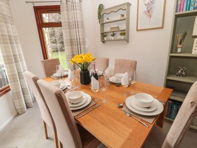 A dining room with a wooden table set for six people and a vase of yellow flowers on the table at Evergreen Lodge in Felmoor Holiday Park near Felton