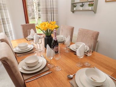 A dining table set with white bowls plates glassware and yellow flowers in a black vase at Evergreen Lodge in Felmoor Holiday Park near Felton