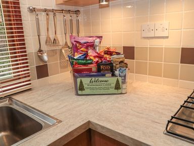 A kitchen countertop with a welcome snack basket near a sink and stove at Evergreen Lodge Felmoor Holiday Park near Felton