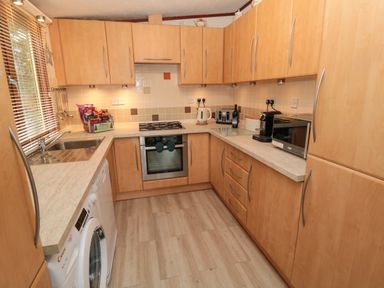 A kitchen with wooden cabinets washing machine oven stove microwave kettle and coffee machine at Evergreen Lodge in Felmoor Holiday Park near Felton