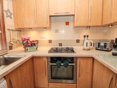A kitchen with wooden cabinets, a gas stove, an oven, a kettle, a toaster, a sink, and snacks on the counter at Evergreen Lodge in Felmoor Holiday Park near Felton