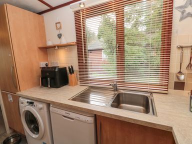 A kitchen counter with a stainless steel sink a washing machine a dishwasher a black appliance and a set of knives at Evergreen Lodge Felmoor Holiday Park near Felton