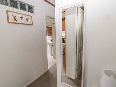 A hallway with a framed picture of animals on the wall and a mirror reflecting an open door at Evergreen Lodge in Felmoor Holiday Park near Felton