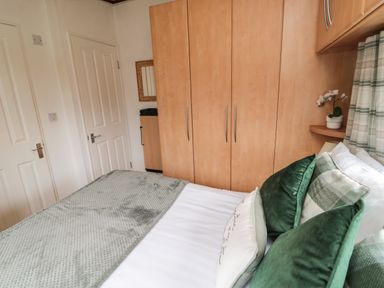 A bedroom with a bed with green and white pillows wooden wardrobes and a small mirror on the wall at Evergreen Lodge Felmoor Holiday Park near Felton