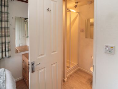 A view of a bathroom with a shower and a dresser visible through a partially open door at Evergreen Lodge Felmoor Holiday Park near Felton
