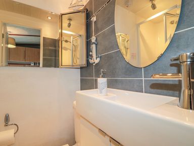 A bathroom sink with a soap dispenser and round mirror above at Evergreen Lodge Felmoor Holiday Park near Felton