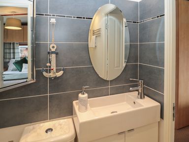 A bathroom with a white sink and faucet an oval mirror and a wall decoration shaped like an anchor at Evergreen Lodge Felmoor Holiday Park near Felton