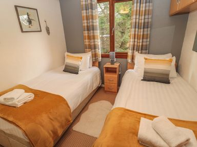 A small bedroom with two single beds a wooden nightstand and a window with plaid curtains at Evergreen Lodge Felmoor Holiday Park near Felton