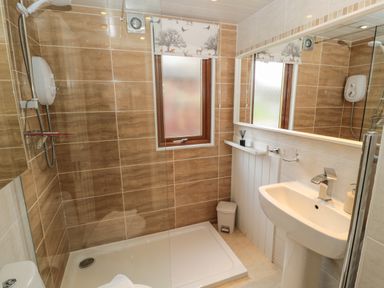 A bathroom with a shower area a sink a mirror a window and a waste bin at Evergreen Lodge Felmoor Holiday Park near Felton