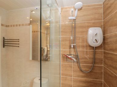 A bathroom with a shower area tiled in brown and beige with a white electric shower and a glass divider at Evergreen Lodge Felmoor Holiday Park near Felton