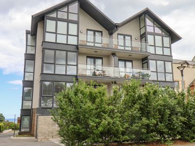 A modern three-story building with large windows and balconies behind green bushes at The Penthouse in Scarborough