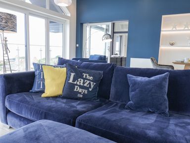 A blue sofa with cushions in a room with large windows and blue walls at The Penthouse in Scarborough