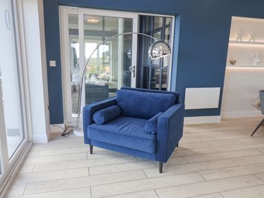 A blue armchair with cylindrical pillows near a floor lamp and glass doors in a room with wooden flooring at The Penthouse in Scarborough