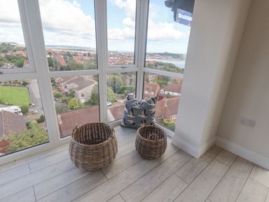 A corner with large windows overlooking houses with two wicker baskets and a cushion on a wooden floor at The Penthouse in Scarborough