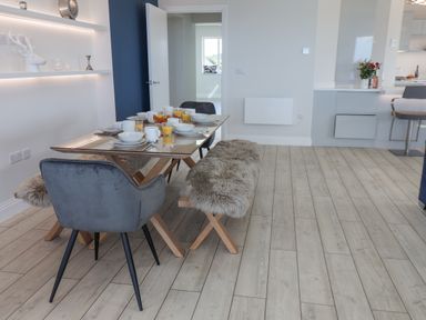 A dining area with a table set for breakfast with gray chairs and a fur-covered bench at The Penthouse in Scarborough