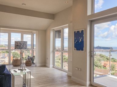 A corner of a room with large windows a glass door side table with a lamp and baskets near the window at The Penthouse in Scarborough