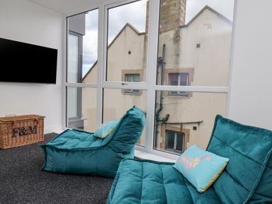 A room with two blue lounge chairs a wicker basket and a wall-mounted TV at The Penthouse in Scarborough