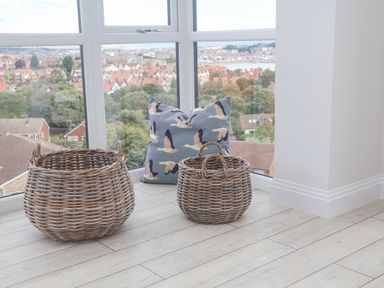 Two wicker baskets and a cushion with a bird pattern near large windows overlooking a residential area at The Penthouse in Scarborough