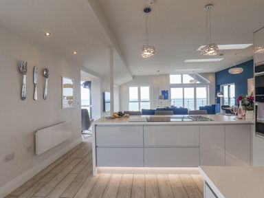A kitchen with a white island and stools overlooking a living room with blue sofas and large windows at The Penthouse in Scarborough