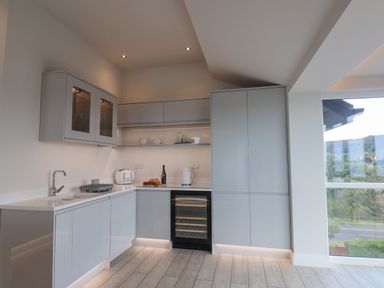 A modern kitchen with white cabinets a sink a toaster a wine cooler and large windows at The Penthouse in Scarborough