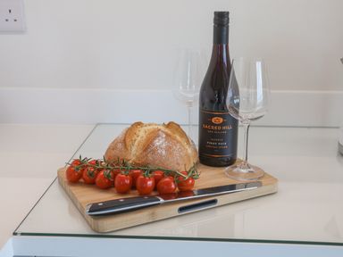 A wooden cutting board with bread cherry tomatoes a knife a bottle of wine and two empty wine glasses on a kitchen counter at The Penthouse in Scarborough