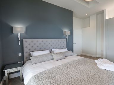 A bedroom with a bed with a grey headboard bedside tables and wall lights at The Penthouse in Scarborough