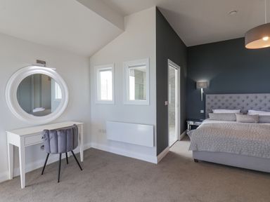A bedroom with a bed against a dark wall and a vanity table with a round mirror and chair at The Penthouse in Scarborough