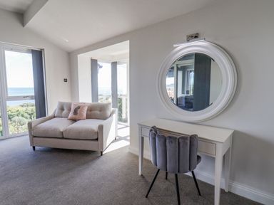 A room with a small beige sofa with a pillow and a white desk with a round mirror above it at The Penthouse in Scarborough