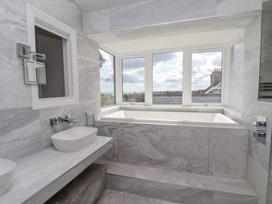 A bathroom with a bathtub under windows and a countertop with two sinks at The Penthouse in Scarborough